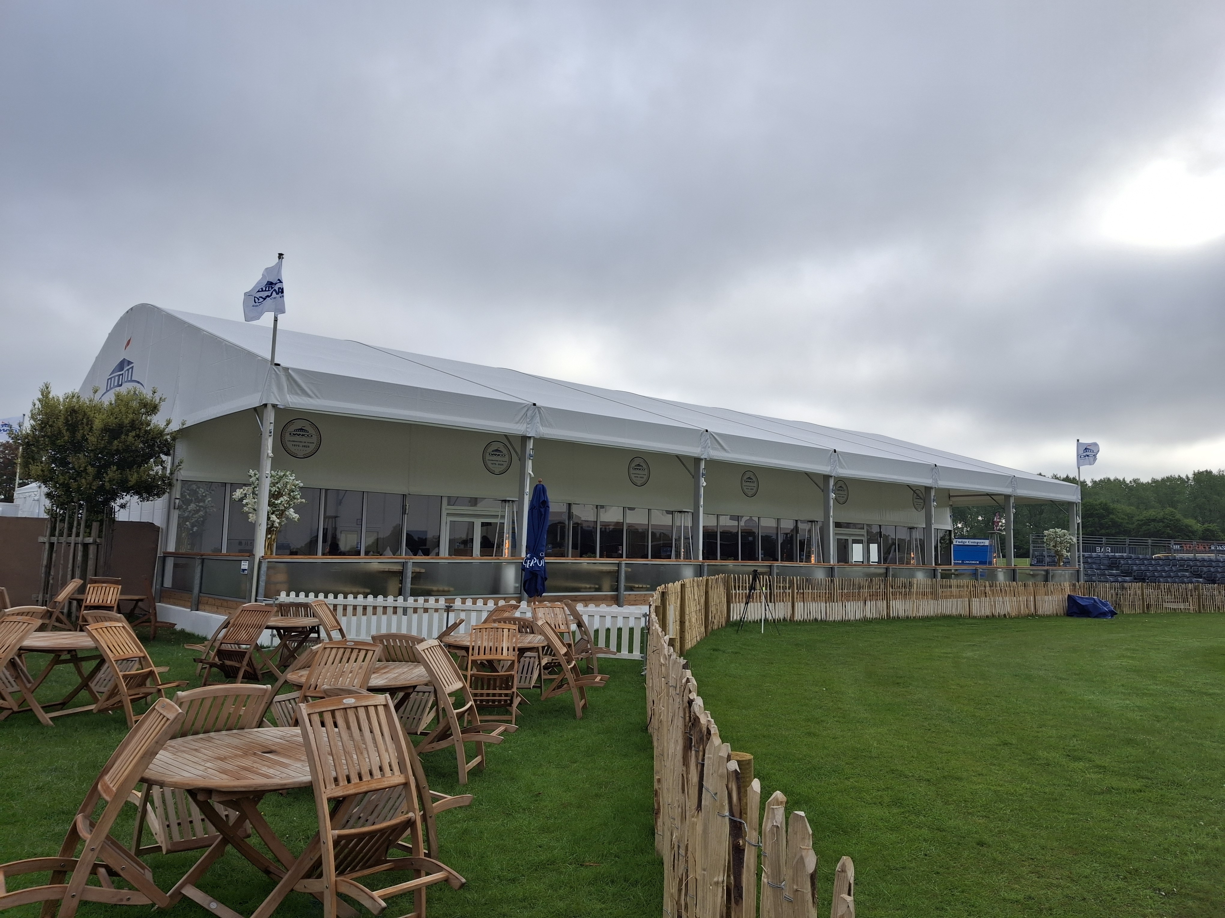 30m long curved roof marquee looking at th balcony with wooden furniture in front on the grass