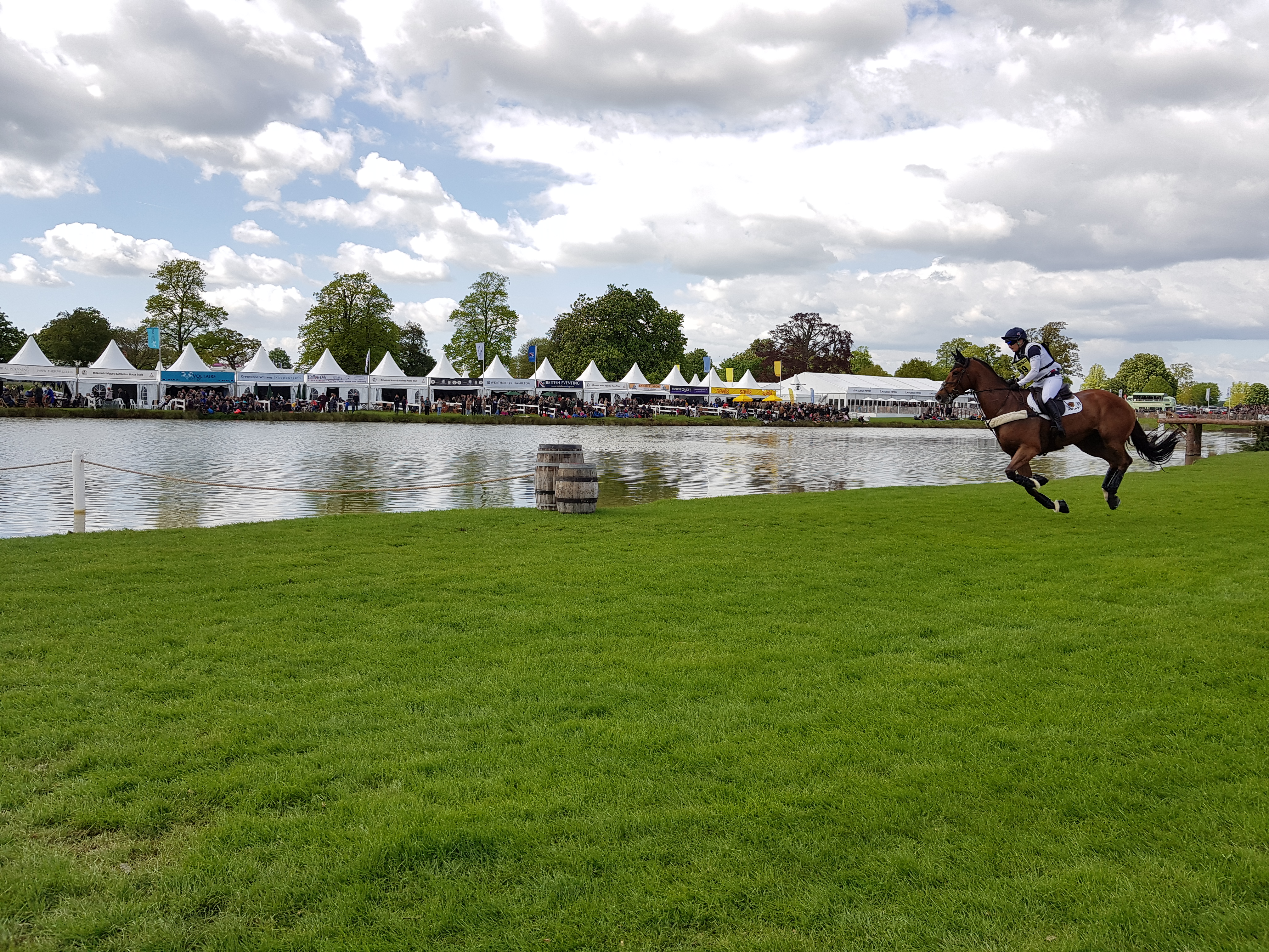 Cross country horse and rider at Badminton horse trials riding past the last with Danco marquee hats in the background. 