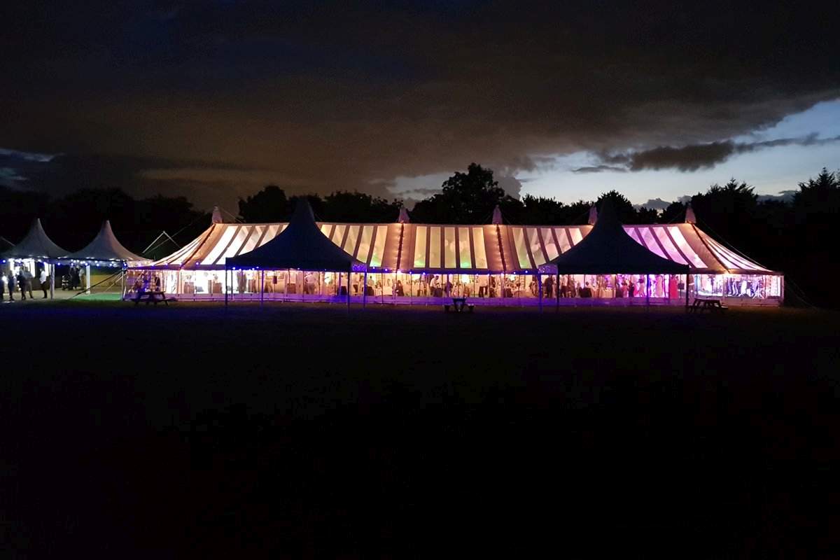 Traditional marquee with semi clear roofs and clear walls lit up at at night 